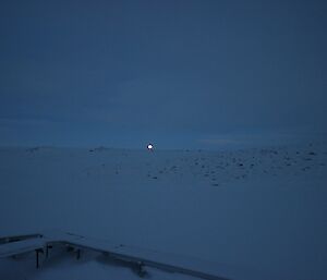 The moon setting over a snowy and rocky terrain