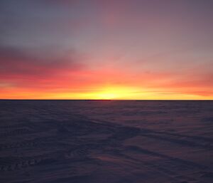 Sunrise over the skiway with high cirrus clouds with scattered light over a flat snow terrain