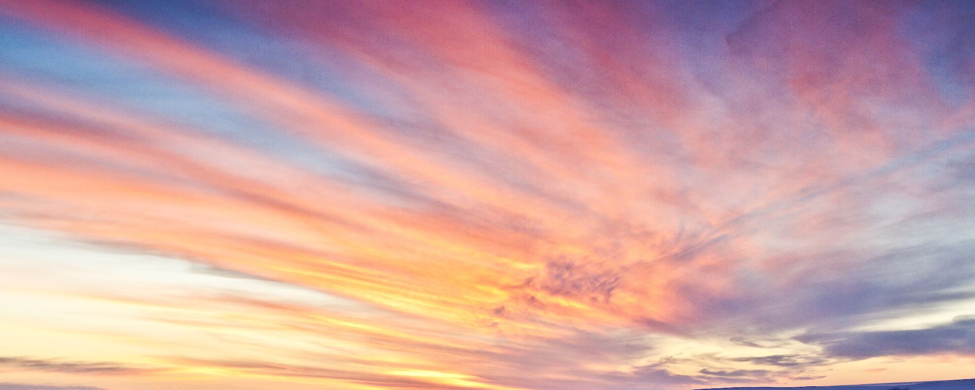 A colourful sunrise with high streaks of thin clouds with a mixture of blue, violet, pink, red and yellow hue across the sky
