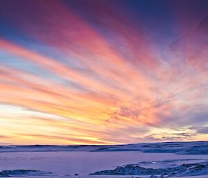 A colourful sunrise with high streaks of thin clouds with a mixture of blue, violet, pink, red and yellow hue across the sky