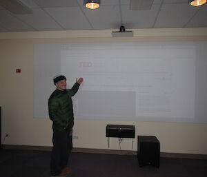 Chad standing in front of the screen holding his hand up introducing the first talk