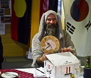 Gavin in a dog suit showing his gift of a wooden clock shaped as Antarctica