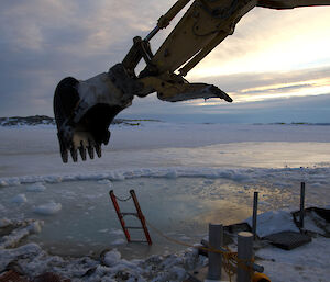 A large digger scrapping ice forming off the water