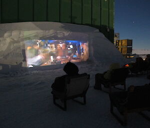 A large movie screen carved out of a snow drift behind the green store building