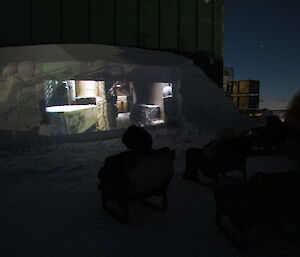 Again a large screen carved from a snow drift behind the green store with a movie playing with people seated in front