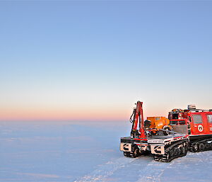 Colourful sunrise sky of pink and baby blue with a red Hägglunds in a flat snowy terrain