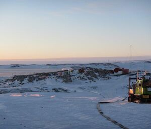 A snowy terrain with a flat long black hose running to the distance with a green hagg on the right