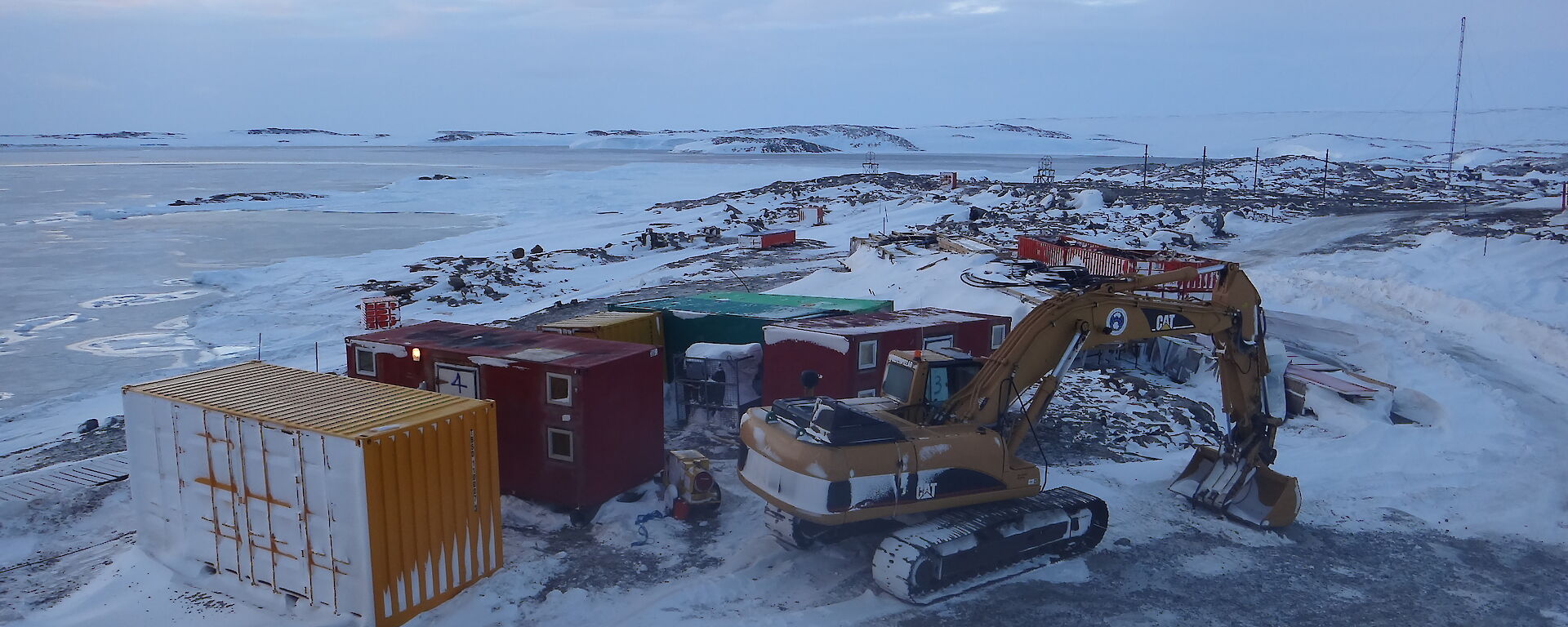 View from the lower fuel farm of the frozen sea ice in the background and shipping crates and excavator in the foreground