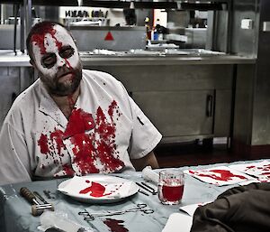 Scotty sitting down in front of the coffee table in a zombie make up with fake blood