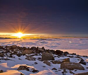 Cloudy sunset with snow and rocky terrain in the foreground with sea ice and icebergs in the background