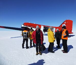 Red twin prop. tail dragger aircraft on snow covered runway with passengers dismounting the aircraft