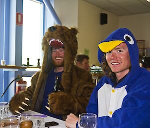 Nick in a brown bear suit and Ben in a penguin suit, both sitting at the dinner table