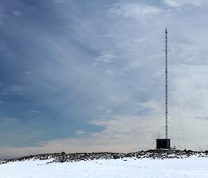 A small hut with long antenna’s on top in a rocky and snowy terrain