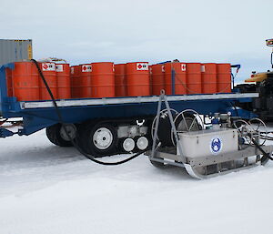 Red fuel drums on a trailer towed behind a tractor.