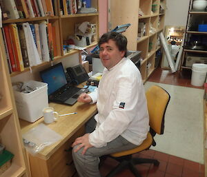 Eddie, the wintering Casey chef, sits on a stool in uniform