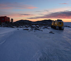 Two expedtioners outside Robbos Hut looking st sunset