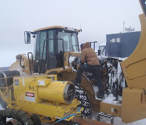 An expeditioner removing snow from inside the engine bay of a loader