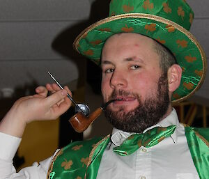 Scott Clifford poses with a dart, dressed as a leprechaun with a green top hat, a wooden pipe hanging out of his mouth