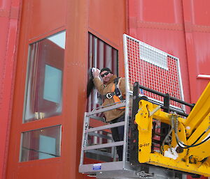Scott Clifford cleaning a window while suspended in a cage on the telehandler outside the red shed at Casey