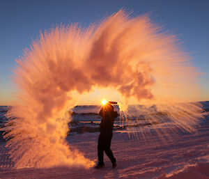 A cup of hot water thrown into the air immediately vapourises and is captured by the camera as a spray of coloured cloud