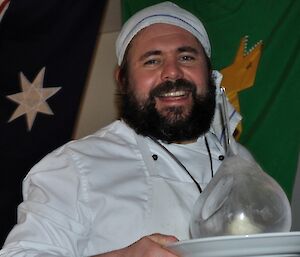 Chef Eddie shows off his iced igloo dessert — he has a dark beard and big smile