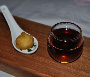 Chicken consomme in a glass and tempura mousseline on a white ceramic spoon-dish