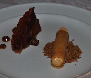 Foie gras cigar with crispy prosciutto, burned fig gel and ginger soil arranged artistically on a plate