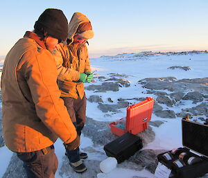 Two expeditioners look at the new filters in their cases on the ground