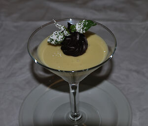 A martini glass filled with white chocolate mousse, topped with mint leaves and chocolate