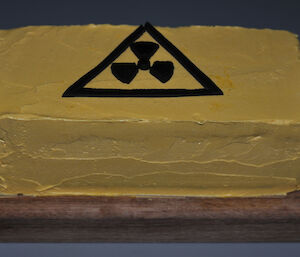 Close up of a square yellow cake with a hazard sign drawn on with icing on top