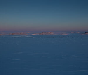 A landscape photo of Antarctica showing low landmasses jutting out from the snow