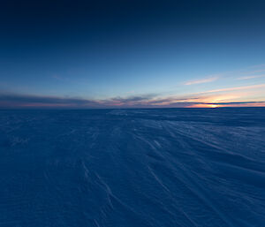 Sunset on the way to Wilkins in Antarctica shows a flat expanse of snow and ice with a touch of sun on the horizon