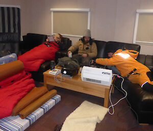 Inside Wilkings mess, near Casey station, Antarctica, three expeditioners try to keep warm in the living room area
