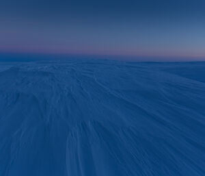 Sunrise over the Wilkins plateau, near Casey station, Antarctica, shows the windblown ice and snow bathed in deep blue light