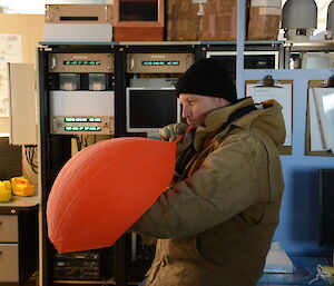 An expeditioner attempts to inflate a weather balloon with lung power.