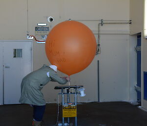An expeditioner inflates a weather balloon at Casey station, Antarctica
