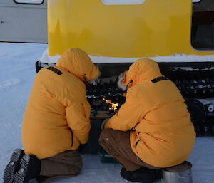 Expeditioners attempt to start a stove alongside a Hägglunds vehicle in very cold conditions