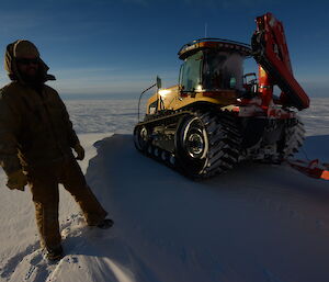 An expeditioner standing next to the Challenger tractor, on the Antarctic tundra