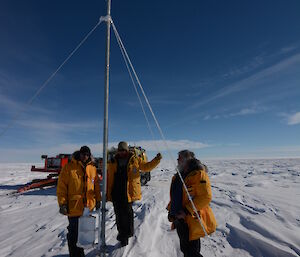 Three expeditioners inspect the automated weather station at Law Dome, partially buried in snow