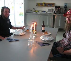 Two expeditioners sit down to a candlelit dinner set up by fellow expeditioners as a joke when they are late back to station