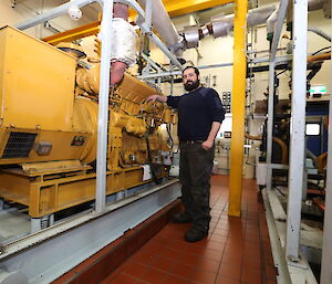 An expeditioner poses next to one of the large diesel engines that powers Casey station