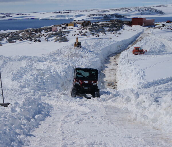 A polaris tracked vehicle drives through the large open-cut road leading to the Casey wharf.