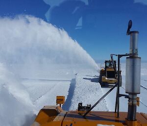 Two machines blow snow from the surface of the runway, on a clear day at Wilkins