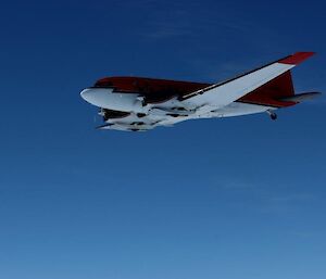 A Basler aircraft taken from below with skis retracted, against a blue sky