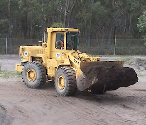 A front loader with a bucket full of soil driven by an expeditioner during training.