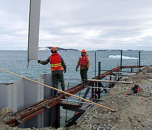 Two men lower a piece of shutter into place to build the wall form.