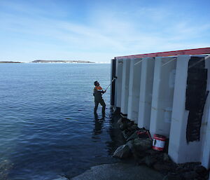 A man stands in the water painting Davis Wharf with a long roller