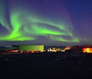 A large green aurora lights up the sky over Davis station