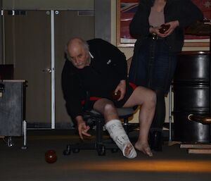 Playing carpet bowls at Davis — Steve sitting down with leg in cast, bowls the ball