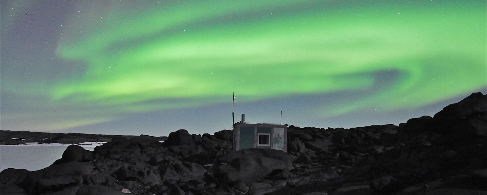 The Aurora Australis fills the sky. Bandits hut in the foreground